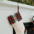 Close-up of a cream Christmas stocking with a red, yellow, and blue tartan cuff hanging from a white mantel decorated with greenery.