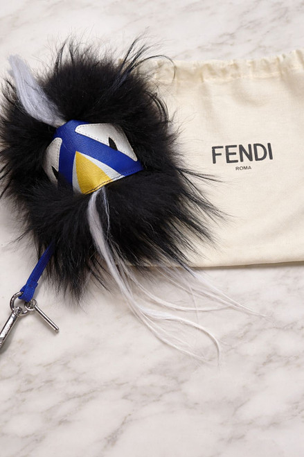 Fendi Monster Bag Charm front top view on white surface with blue & yellow face, black & white hair with Fendi dust bag