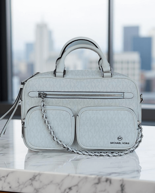 Michael Kors Elliot Messenger Bag front in off-white, top handles raised, 3 front zip compartments & MK monogram finish