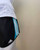 Adidas Black Running Shorts – side view showing light blue three-stripe detail & curved hemline under white top