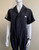 Adidas x Fiorucci Black Boiler Suit closer front view with short sleeves, Fiorucci chest logo, zip-up front with flap over