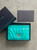 Prada Turquoise Leather Card Holder front view in open black Prada box with lid & Prada envelope to the side