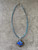 Square Glass Flower Pendant Necklace full top view with teal cord & dark floral pendant with bold blue flower contrast