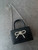 Black Crossbody Mini Bag with Bow Detail flat lay in almost square shape, top handle & silver bow on flap & silver chain