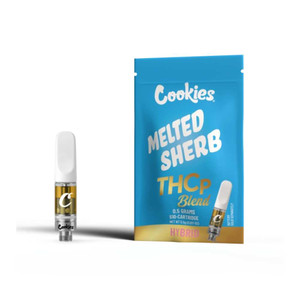 A clear 1 g vape cartridge labeled “Cookies” stands next to its bright blue packaging featuring bold white text reading “Cookies THC‑P Taste” and playful strain artwork; the cartridge shows golden oil inside a glass chamber and a silver 510-thread base topped with a white mouthpiece A clear 1 g vape cartridge labeled “Cookies” stands next to its bright blue packaging featuring bold white text reading “Cookies THC‑P Taste” and playful strain artwork; the cartridge shows golden oil inside a glass chamber and a silver 510-thread base topped with a white mouthpiece