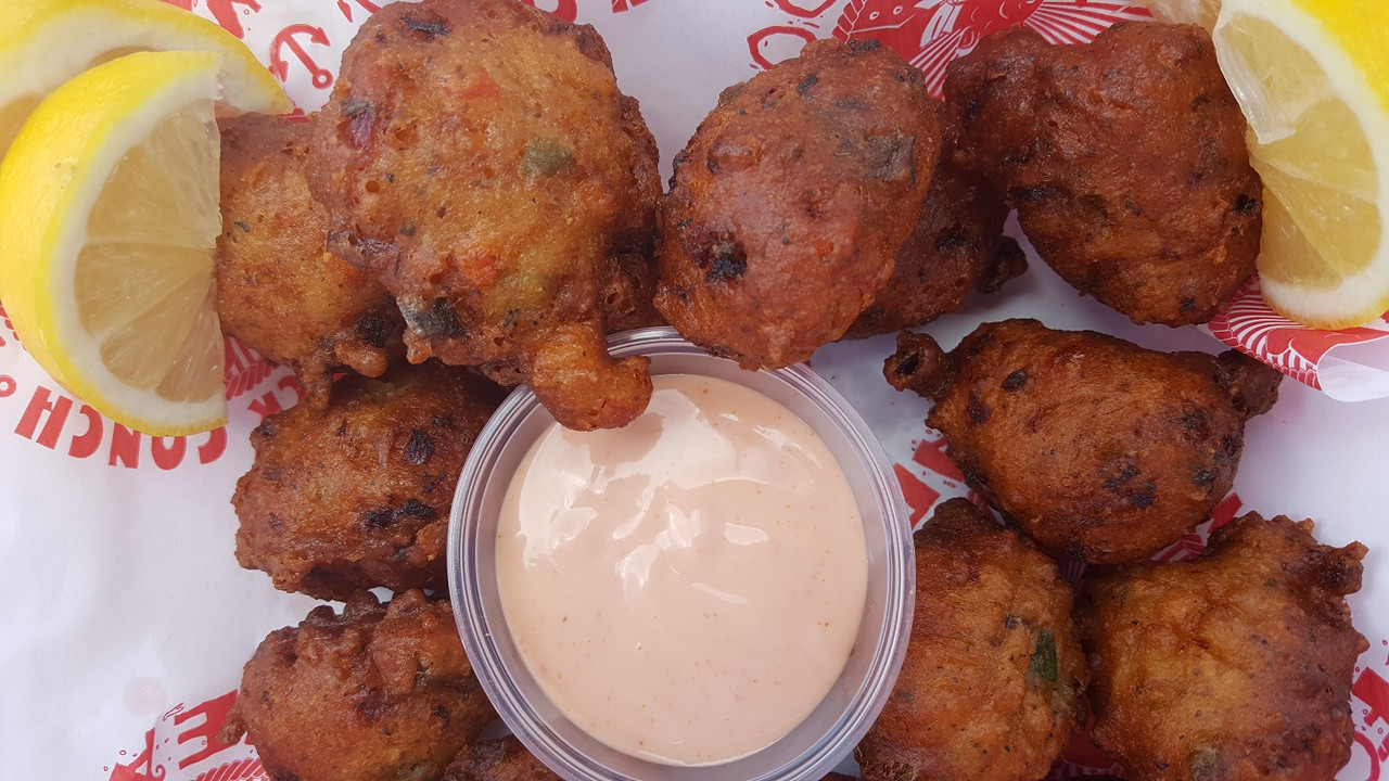 conch fritters in basket with lemon and dipping sauce