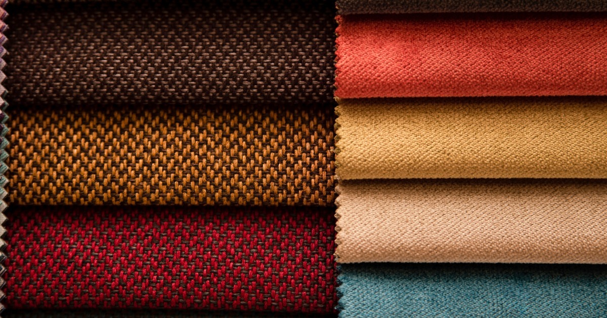 Close-up of two stacks of woven and solid upholstery fabric. They include shades of brown, red, tan, beige, and blue.