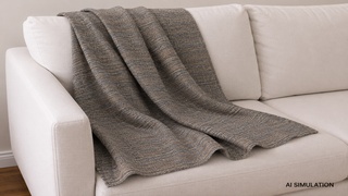 AI-generated simulation of gray and brown textured woven upholstery fabric draped across a cream sofa, showing the multi-tonal woven pattern, dimensional texture, and natural fabric folds in a styled interior setting. The image is a digital visualization created from an actual fabric photograph and is intended to demonstrate color, pattern, and general appearance.