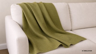 AI-generated simulation of olive green woven plain upholstery fabric draped across a cream sofa, showing fabric color, weave texture, and natural folds in a styled interior setting. The image is a digital visualization created from an actual fabric photograph and is intended to demonstrate color, pattern, and general appearance.
