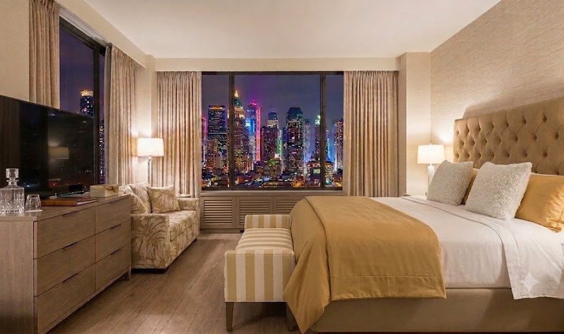 Upscale luxury hotel room featuring hospitality contract upholstery fabrics on a tufted faux leather headboard, striped bench, palm-patterned seating, and coordinating decorative pillows.