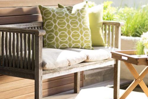 Outdoor bench with light seat cushions and green patterned pillows illustrating Outdura indoor outdoor upholstery fabric