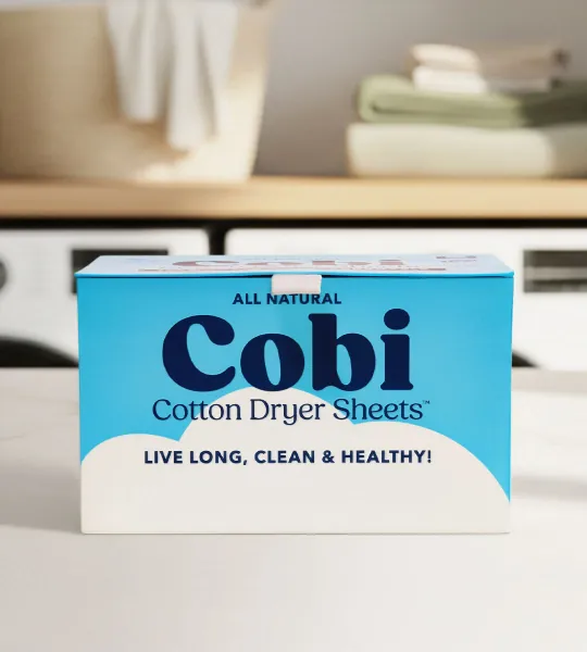 Stack of folded laundry topped with a box of Cobi Cotton Dryer Sheets