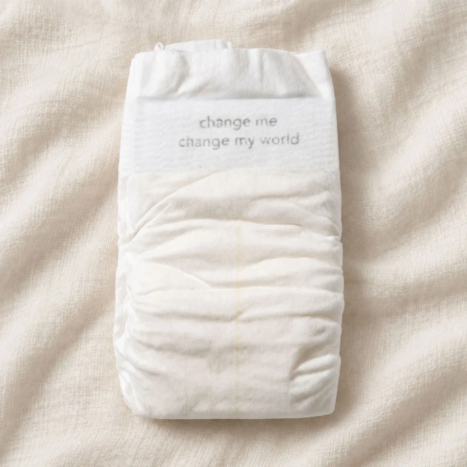 A single Change cotton diaper on cream muslin, printed with “change me, change my world” on the waistband.