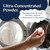 Hand holding a container of ultra-concentrated powder in front of an open washing machine with text about precision dosing and peak performance.