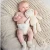 Baby lying on a chunky knit cream blanket, wearing a natural Change Diapers diaper and knit booties, holding a cream stuffed bunny toy.