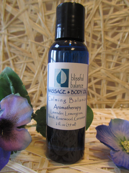 Massage body oil in a blue Blissful Balance bottle with purple silk flowers