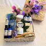 Our  handmade Lupis basket filled with bath and body products, including blue and white  plastic bottles and jars, eye gel mask, pumice brush, aromatherapy soap decorated with pink and purple flowers.