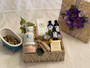 Straw colored Lidded basket filled with blue and white bottles and jars. Aromatherapy products with essential oil. Headband and pumice brush included, with lid decorated with silk flowers and ribbon.