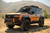 A copper-colored 2024 Toyota Land Cruiser 250 in the dessert featuring a DV8 roof rack kit. A copper-colored 2024 Toyota Land Cruiser 250 in the dessert featuring a DV8 roof rack kit.