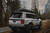 A rear view of a white LC 250 Land Cruiser in the forrest on a trail with a DV8 roof rack. A rear view of a white LC 250 Land Cruiser in the forrest on a trail with a DV8 roof rack.