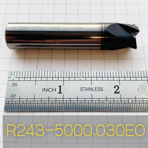 Refurbished End Mills R243-5000.030EO, tapered cylindrical metal cutting tool with cutting edges, placed on grid paper with ruler for scale.