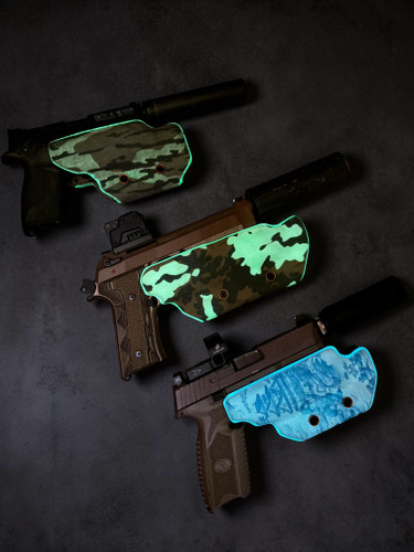Three suppressor-friendly OWB holsters displayed on a dark background, showcasing glow-in-the-dark dual-layer construction. The top holster features an M81 camouflage wrap with green glow trim, the center holster features a black and green glow pattern, and the bottom holster features a blue topographic glow finish. All three holsters are configured for red dot optics, suppressor use, and open-top light-retention carry.