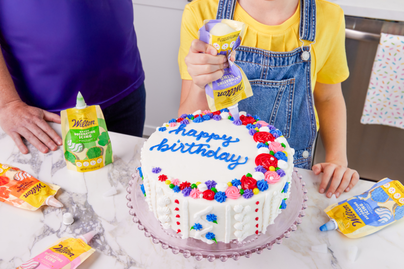 Colorful birthday cake being decorated with Wilton's icing pouches with versatile decorating tips.