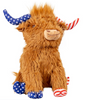 A front product photograph of a shaggy brown Highland cow plush pet toy set against a white background. This patriotic stuffed animal features mismatched Americana-themed accents, with its right horn and hooves styled in a blue-and-white star pattern, and its left horn and hooves styled in red-and-white stripes.
