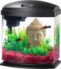A front product photograph of a small bowfront desktop aquarium with a black hood and base, featuring a Buddha head ornament, pink gravel, and two yellow and black fish, isolated against a white background.