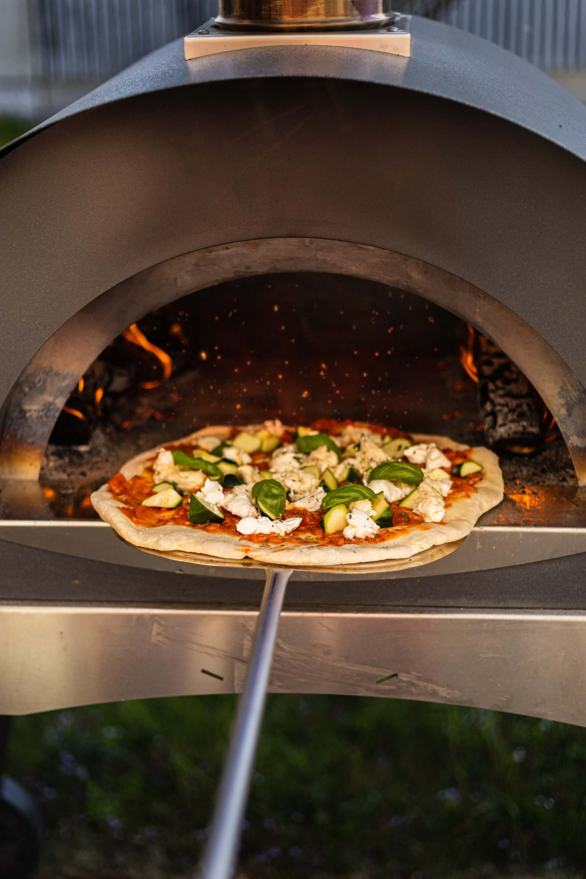 Delicious margherita pizza being placed in flaming pizza oven