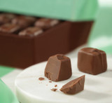 Hover - Profile view of Milk Mint chocolate piece cut in half with box of chocolates in the background