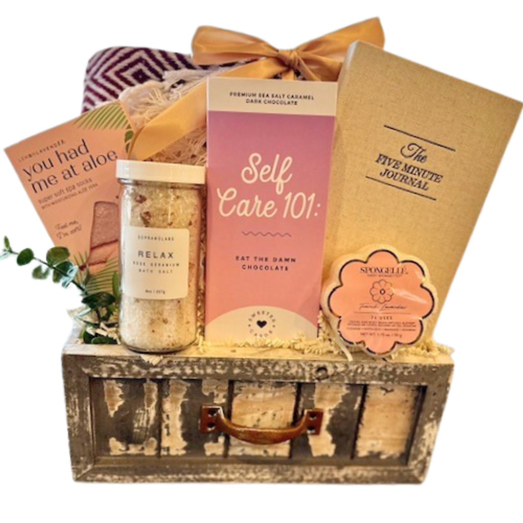 Cozy up in this self care gift basket.  Perfect for anyone who is in need of a little comfort. Created in a wooded drawer includes a woven cotton blanket, plush aloe socks, relaxation bath salts, a five minute motivational journal and a spongelle infused sponge.