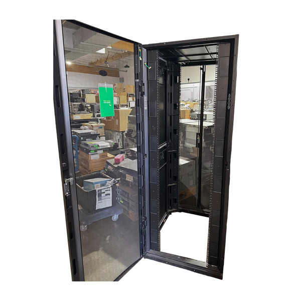 A front view of an open black APC server rack enclosure with its perforated mesh front door swung completely open, revealing a hollow internal frame and a warehouse background, isolated on a black background