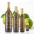 Family of Tarpon Springs Olive Oil Company green lemon extra virgin olive oil bottles in four sizes: 750ml, 375ml, 250ml, and a small tasting bottle. Each dark glass bottle has a gold cap and the company’s white etched harbor-scene label. Fresh whole green lemons, green leaves, and a cut lemon sit behind the bottles on a bright white background, highlighting the citrus flavor of the oil.