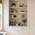Pine alcove floating shelves with natural wood grain installed between white cabinetry above a kitchen coffee bar.
