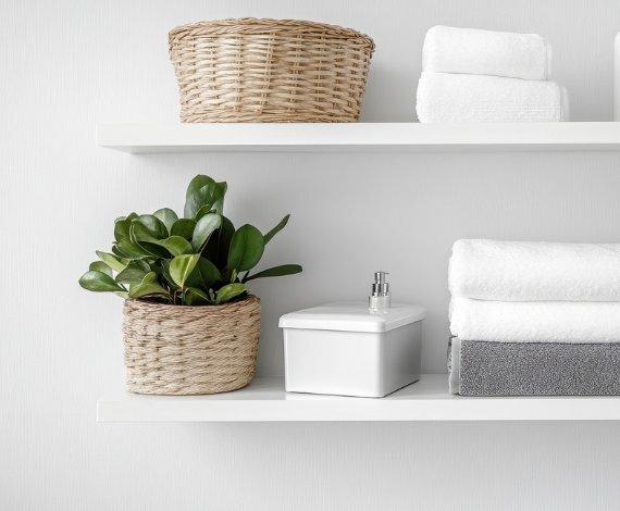 White painted floating shelves, 1.625 inches thick, styled with bathroom accessories, potted plants, and woven baskets for storage