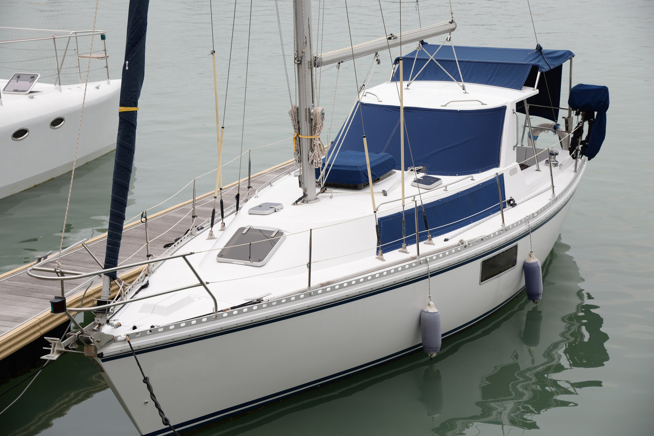 A sail boat docked with its sails furled and blue covers on the cab area