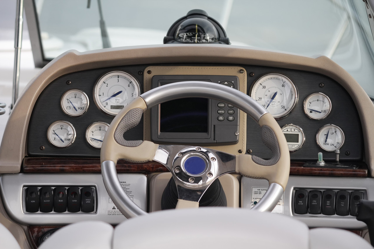 The dash of a boat with the steering wheel and all the gauges and dials with a bubble compas 