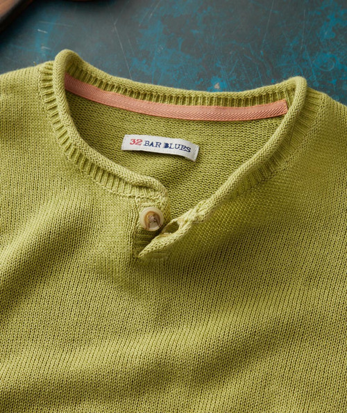 32 Bar Blues Brand-New Life, close-up of a lime green knitted sweater with a pink trim on the collar and a white button.