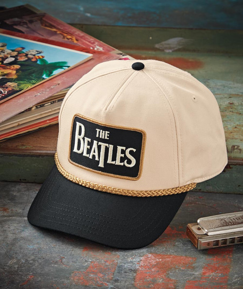 32 Bar Blues Tell It Like It Is, a beige and black baseball cap with The Beatles logo embroidered on the front, placed on a rustic wooden surface next to vinyl records and a harmonica.