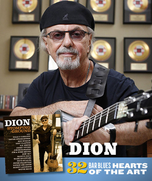 32 Bar Blues Stomping Ground - Dion, image of Dion with guitar in front of gold record plaques, wearing a black beanie and glasses, smiling at the camera.