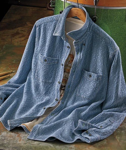 32 Bar Blues Jumpy Blues, a textured blue denim shirt with a snakeskin pattern, featuring two chest pockets with button closures, hanging on a wooden hanger over a rustic surface.
