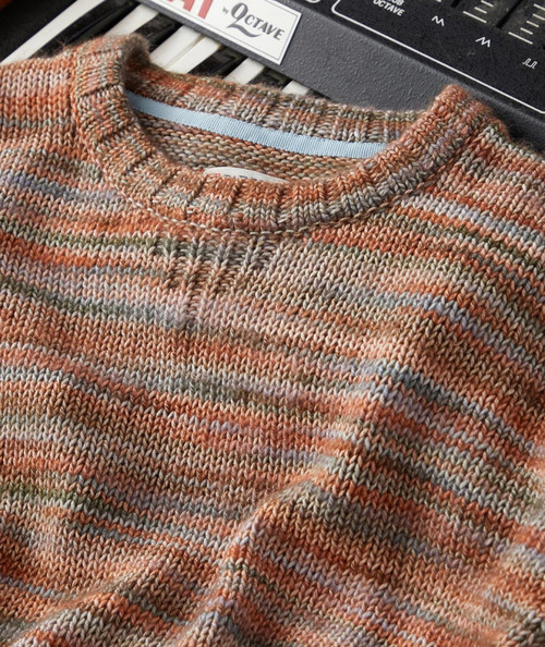 32 Bar Blues Siesta At The Fiesta Sweater, close-up of a multicolored, knitted sweater with a crew neckline made of orange, beige, and gray yarns, laid on a musical keyboard and a synthesizer.