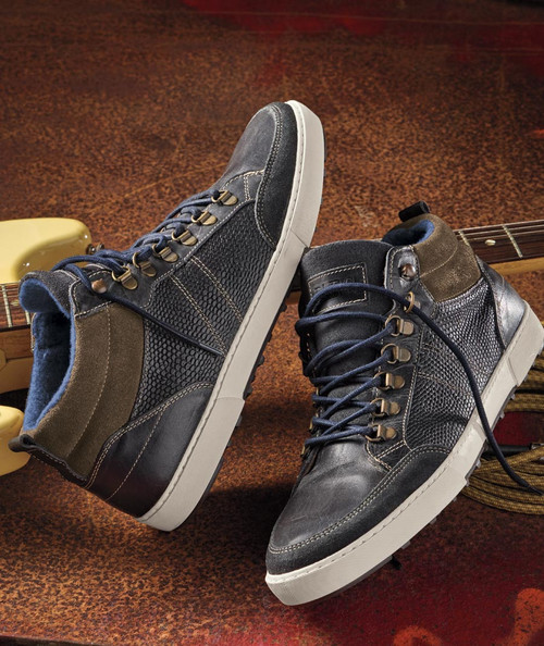 32 Bar Blues The Sidewalk Is Wild, stylish men's sneakers with black and brown textured leather and suede detailing, white rubber soles, and laced closure, on a rustic wooden surface.