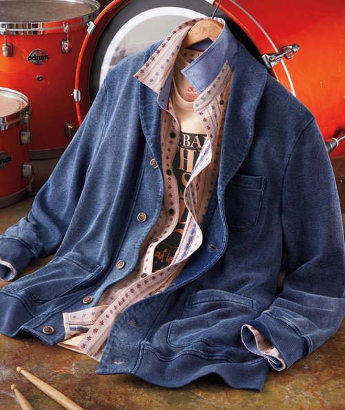 32 Bar Blues Beef Stew Blues, a denim jacket layered over a patterned shirt and a graphic t-shirt, hanging on a hanger in front of orange drums.