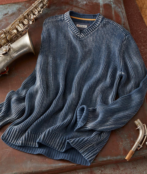 32 Bar Blues Evening Shadows, a blue and gray striped knitted sweater with a V-neck, laid on a wooden surface with a saxophone and a clarinet placed beside it.