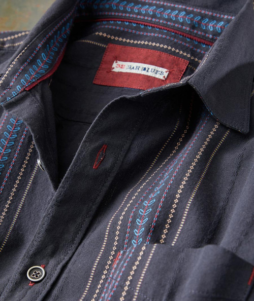 32 Bar Blues Deep Felix, close-up of the dark-colored shirt with intricate red, blue, and beige embroidered lines and patterns, featuring a red and white label inside the collar.