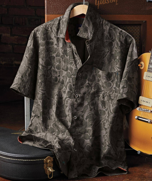 32 Bar Blues I Talk To The Trees, patterned short-sleeve button-up shirt hanging on a wooden hanger against a brick wall with a guitar nearby.