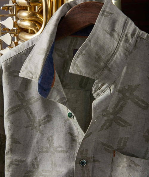 Product 32 Bar Blues Jazzmatazz, close-up of a beige shirt with subtle star and floral patterns, metal buttons, and contrasting inner collar detail, hanging on a wooden hanger.