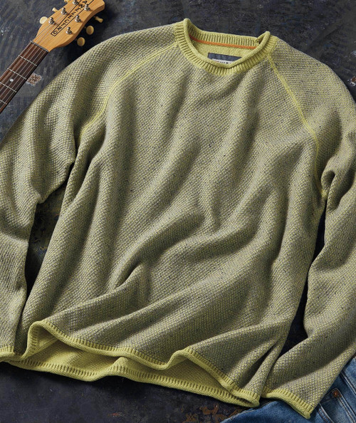32 Bar Blues Honey In The Comb - Pistachio, green textured knit sweater with ribbed collar and hem, laid flat on a dark surface with a guitar and denim jeans visible.